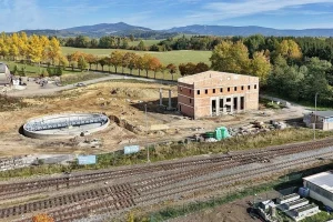 Letecký pohled na staveniště s kruhovou jámou točny a hrubou stavbou budovy u kolejí